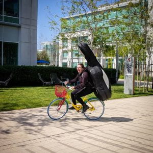 Maya riding a bike at Google campus with upright bass strapped to her back
